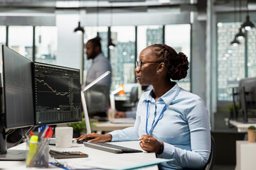 Day trader working for hedge fund company buys and sells stocks to capitalize on market fluctuations. African american woman in prop firm office uses price charts to identify fast profit opportunities