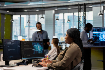System administrator in tech startup uses AI on PC to optimize performance and forecast issues. African american woman in office training machine learning models using computer