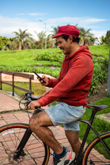 Male cyclist stopped on a bridge in an outdoor park, looking at his phone. He is wearing a cycling...