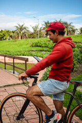 Obraz premium Male cyclist stopped on a bridge in an outdoor park, looking at his phone. He is wearing a cycling cap, a hoody, and shorts, combininga casual and sporty look. 
