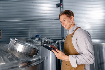 Worker male brewer inspecting equipment in modern brewery setting with stainless steel tanks....