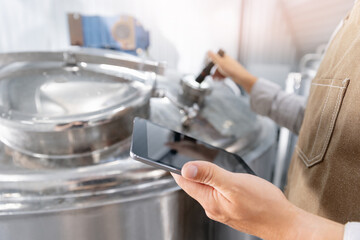 Modern brewery, worker use tablet computer with AI assistant for controlling stainless steel...