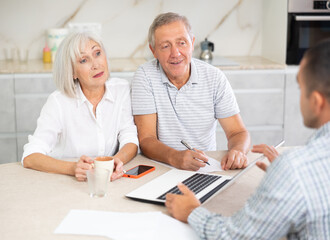 Obraz premium Couple of elderly man and woman discussing deal with male salesman in kitchen home
