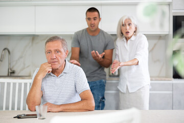 Obraz premium Adult man sits at table and thinks how to resolve conflict with his wife and son