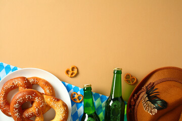 Festive flat lay of pretzels, beer bottles, Bavarian hat with feather, and checkered cloth on tan...