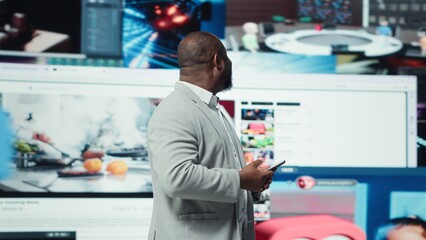 Smiling man using phone gains access to thousands of videos with press of a button. Jolly african american man enjoys free time browsing favorite online clips on smartphone, camera A