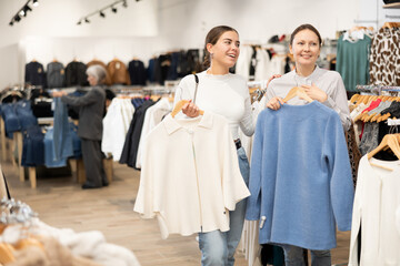 Adult and young women shoppers choose coat in clothing store..