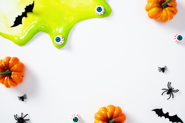 Happy Halloween concept. Creepy green slime with fake eyeballs, pumpkins, bats, and spiders on white background.