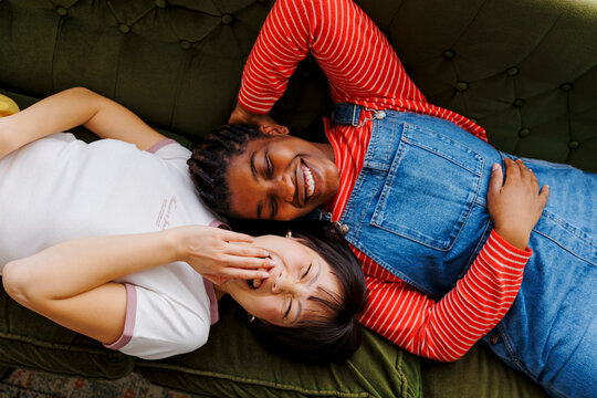 Two happy friends laughing and lying on a green sofa