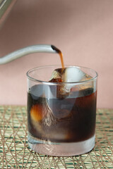Dark roasted  iced coffee being poured into a glass.