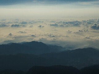Drone view of a breathtaking mountain landscape above the clouds, showcasing rugged peaks and serene valleys in a stunning high-altitude natural scene.