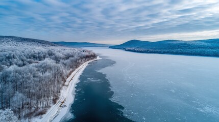Obraz premium Icy River Landscape with Forest and Hills Under a Cloudy Winter Sky Aerial View