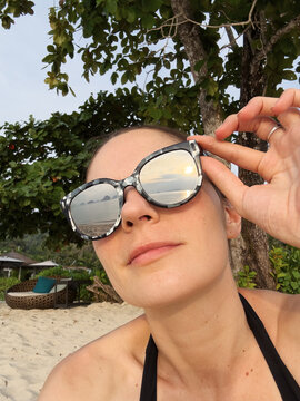 Selfie of a woman in reflective sunglasses with ocean in them