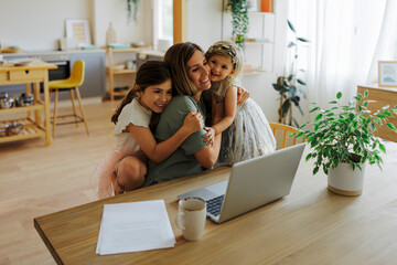 Mother working from home and receiving hugs from daughters