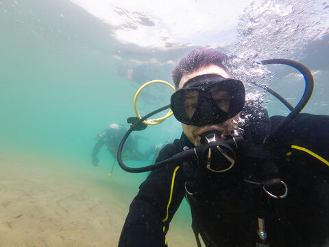 Diver exhaling underwater near sandy seabed with another diver