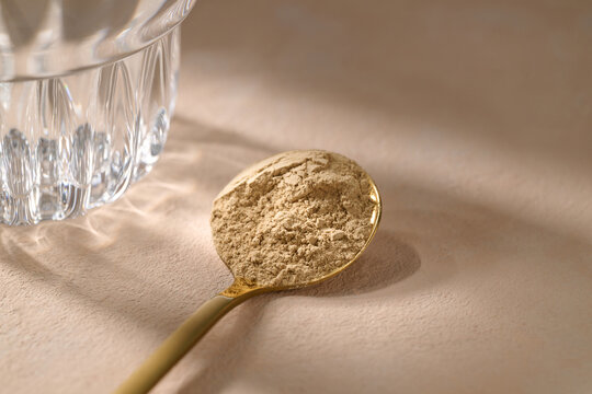 A golden spoon filled with maca powder sits alongside a glass of water