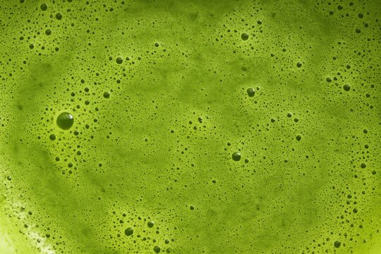 Top view of frothy matcha latte with its signature vibrant green color and delicate swirling foam patterns, a macro and full-frame texture shot, close-up texture