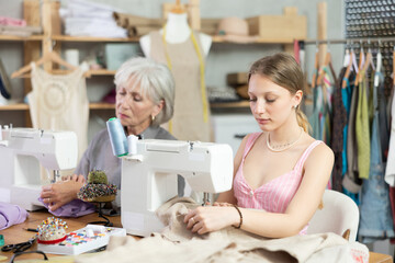 Elderly and young women seamstresses sewing on machine in sewing workshop