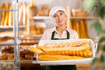 Bakery advertising banner. Senior woman employee works in bakery store, sells baguettes, shows product, brings additional portion of finished product to sales floor
