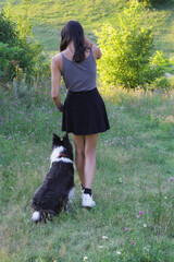 Woman walking with Border Collie dog weaving through her legs during outdoor training session in...