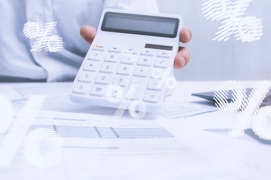 Professional white calculator in hand, above business documents with financial charts and percentage data visualization overlay. Accounting, financial analysis and business planning concept.