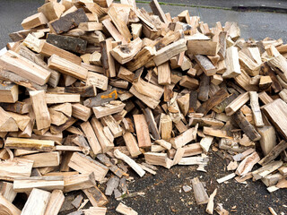 A large pile of freshly split firewood lies scattered across the pavement awaiting stacking for storage and use during the winter heating season