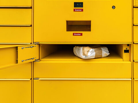 A paper-wrapped parcel placed inside an open yellow locker compartment labeled with scanner and printer sections in a public parcel delivery terminal