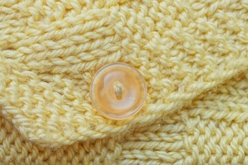 one small plastic brown button on a yellow woolen knitted fabric of clothing