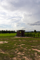 Rustic zinc sheet outdoor toilet standing in lush green rice field beside rural road, simple countryside lifestyle surrounded by nature