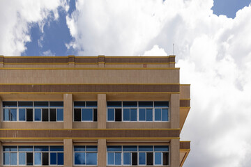 Side view of a contemporary glass building with mirror-like windows reflecting white clouds and a vibrant blue sky on a sunny day.