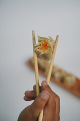 Hand Holding Dim Sum with Chopsticks on White Background