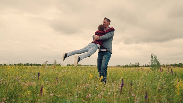 Father spinning son in meadow, joyful outdoor play, happy family bonding in nature, childhood dream of flying, dad and boy playing superhero, fatherhood love and happiness, child laughing in father s