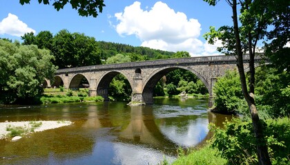 Fototapeta premium Stone arch bridge over river, lush greenery