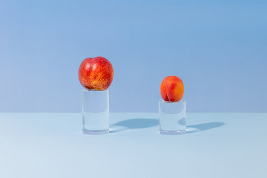 Two peaches displayed on glass pedestals with a light blue background 