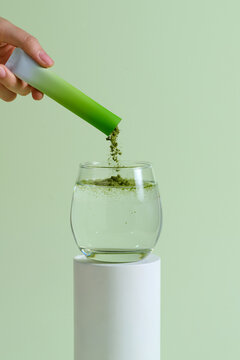 A hand pouring green powder from a sachet into a glass of water