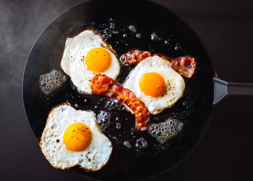 Cooking breakfast with crispy bacon and fried eggs in a skillet