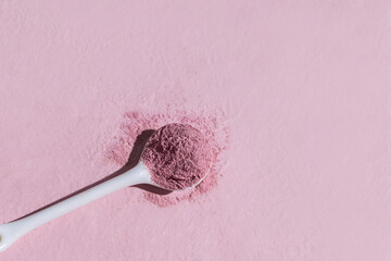 A white spoon filled with pink powdered supplement 