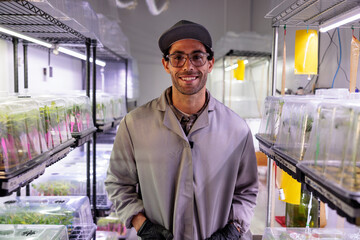 Scientist smiles in indoor vertical farm with plant seedlings.