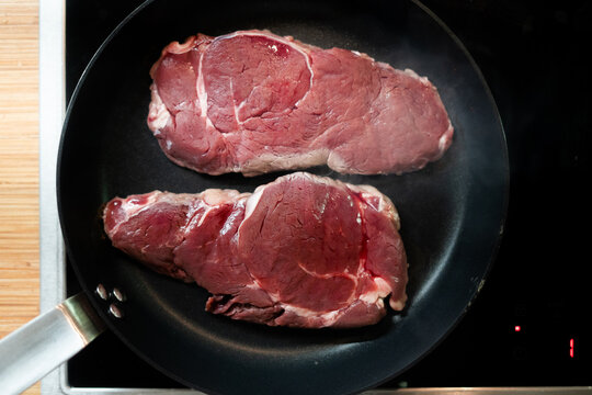 Two raw beef steaks cooking in a hot frying pan