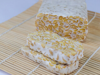 Sliced of Tempeh or tempe on woven bamboo. Tempeh is a traditional Indonesian food made from fermented soy beans. Isolated on white background.
