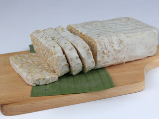 Sliced of Tempeh or tempe on cutting board. Tempeh is a traditional Indonesian food made from fermented soy beans. Isolated on white background.