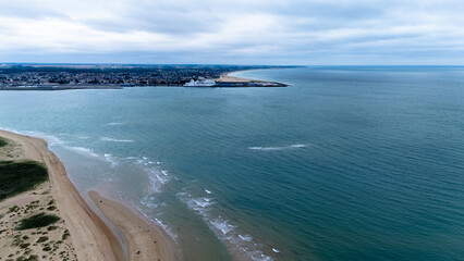 Aerial view of coastal town with sandy beach and calm ocean on overcast day.