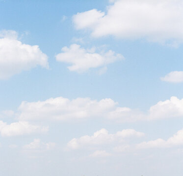 Fluffly white clouds against pale blue sky on film