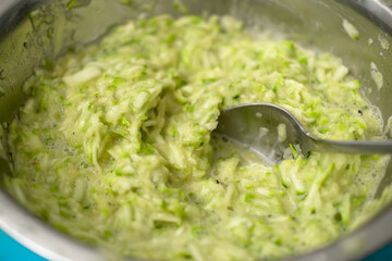 Close-up of grated fresh zucchini in metal bowl with spoon.