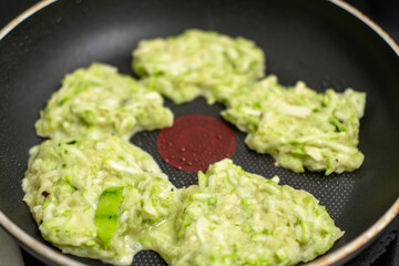 Cooking zucchini fritters in nonstick frying pan with zucchini batter.