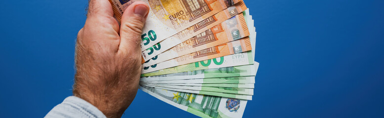 A closeup of a male hand holding a fan of euro banknotes in different denominations against a clean...