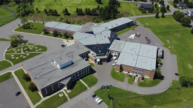 Aerial view of a public secondary school surrounded by green lawns. This school's architecture resembles a crab when viewed from the sky. City of Amqui, Quebec, Canada. 2025.