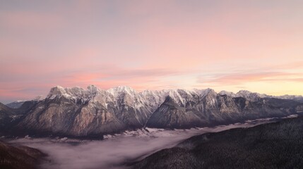 Obraz premium Majestic mountain range at sunrise with soft pink and orange hues over snowy peaks and misty valleys.