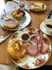 Delicious english breakfast plate featuring fluffy pancakes and crispy bacon served with maple syrup on a decorative floral plate, showcasing a delightful morning meal experience. Vertical background