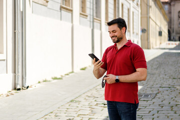 Man enjoys using smartphone while standing on a cobblestone street during daylight